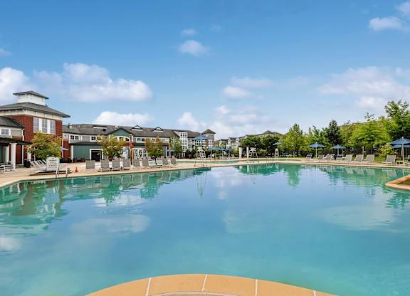 A large swimming pool in front of a building with a blue sky and clouds in the background.