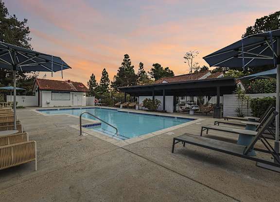 A pool area with sun loungers and a building in the background.
