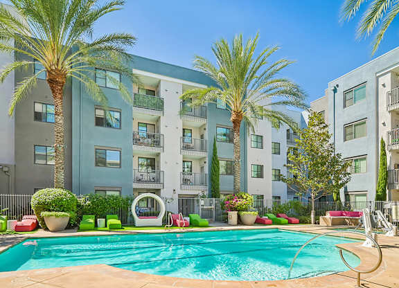 A swimming pool in front of a multi-story apartment building with palm trees.
