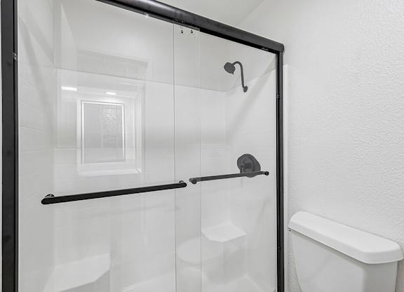 A white toilet is in a small bathroom with a glass shower door.