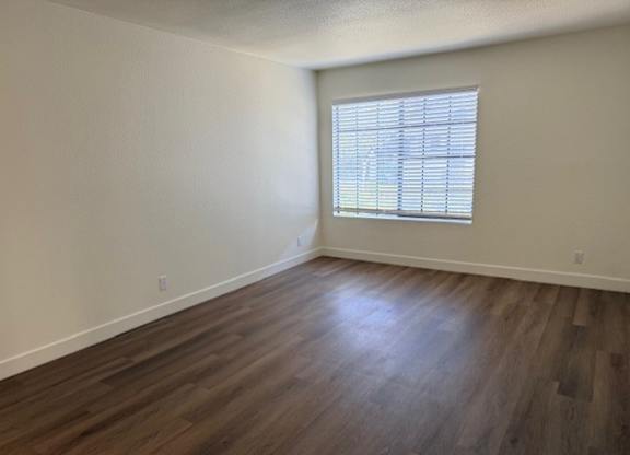 A room with wooden flooring and a window with blinds.
