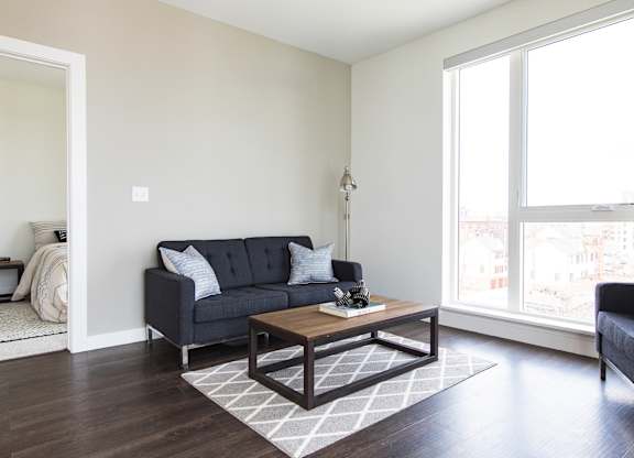A black couch with white pillows sits in a living room with a coffee table in front of it.