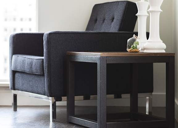 A black chair and table with a white vase on it.