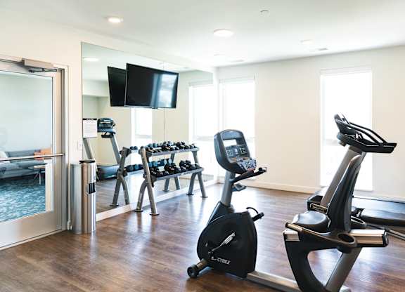 A room with a treadmill, a stationary bike, and a television.