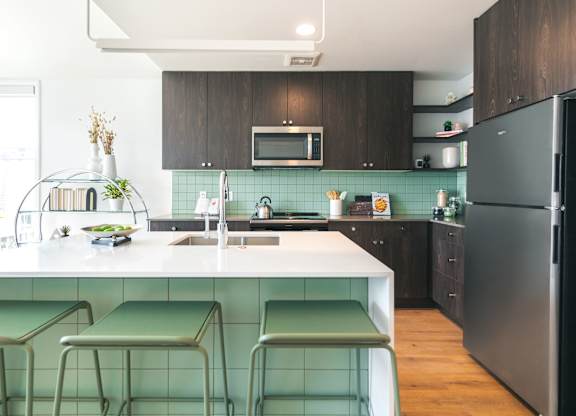 A kitchen with a black refrigerator and green bar stools.