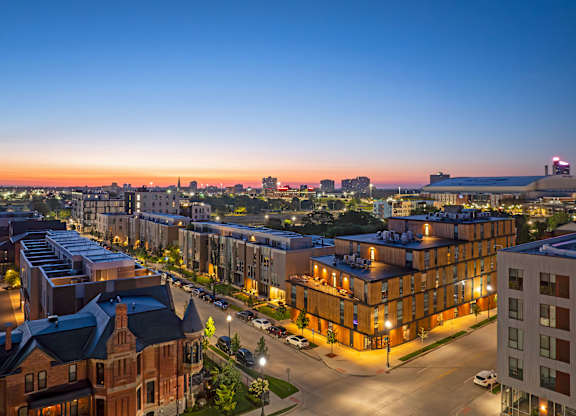 A cityscape at dusk with buildings illuminated and a clear sky.