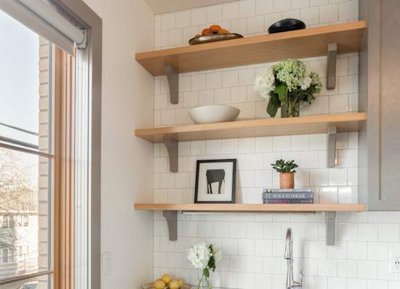 A kitchen with a stainless steel dishwasher and wooden shelves above the sink.