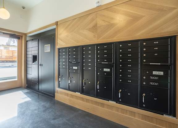 A series of black lockers with numbers on them are lined up against a wooden wall.