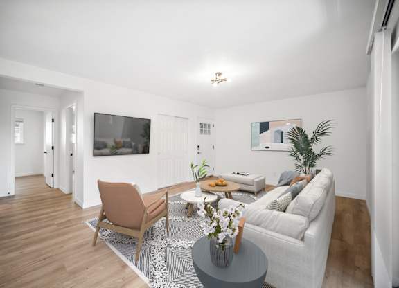 A living room with a grey couch, a brown chair, a coffee table with a vase of flowers, and a flat-screen TV mounted on the wall.