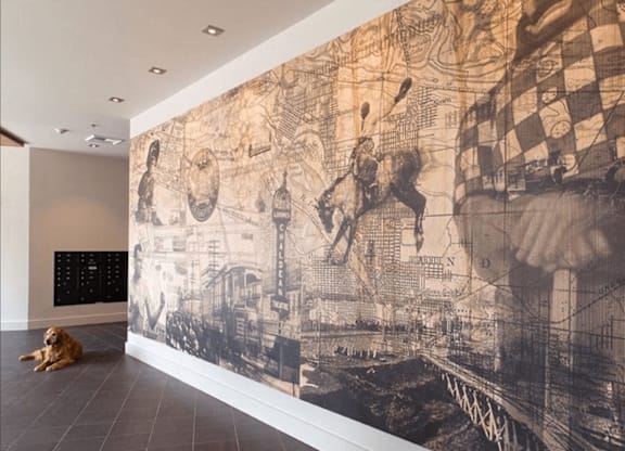 A dog is sitting on the floor in front of a wall with a large black and white mural.