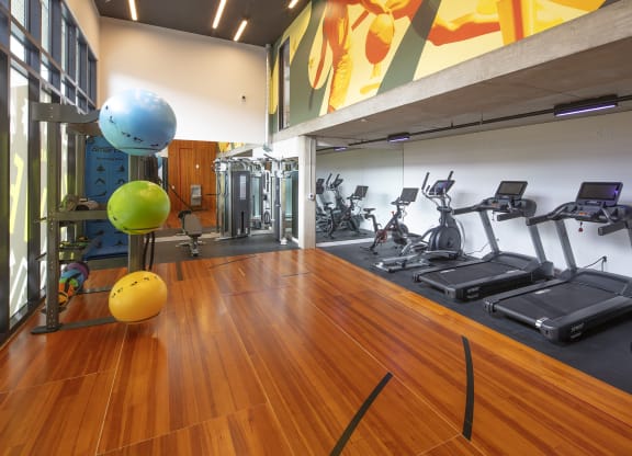 a gym with cardio equipment and weights on a wooden floor at The Weidler in Portland, OR 97209