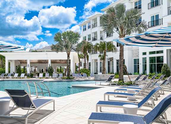 A pool area with sun loungers and a white building in the background.