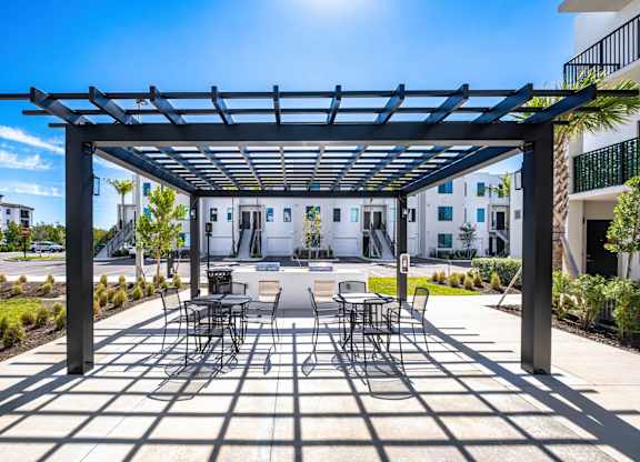 A patio with a table and chairs under a black pergola.