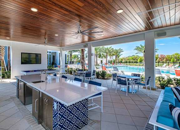 a covered patio with tables and chairs and a swimming pool at Altis Twin Lakes Apartments, Kissimmee, FL