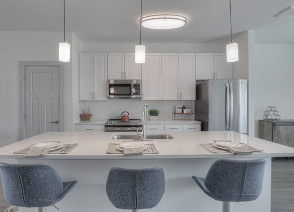A modern kitchen with a white island and grey chairs.