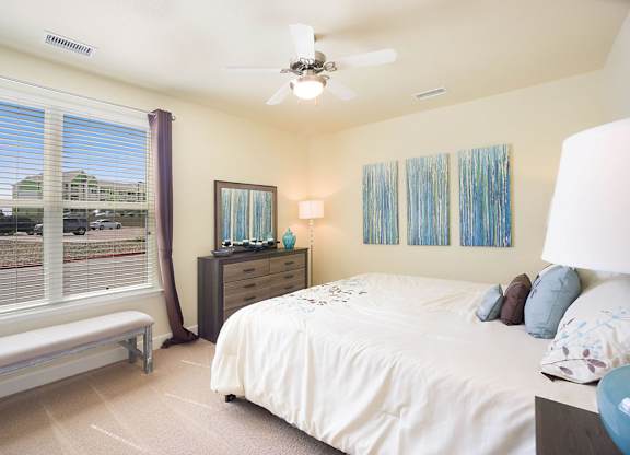 A bedroom with a bed, dresser, and window with blinds.