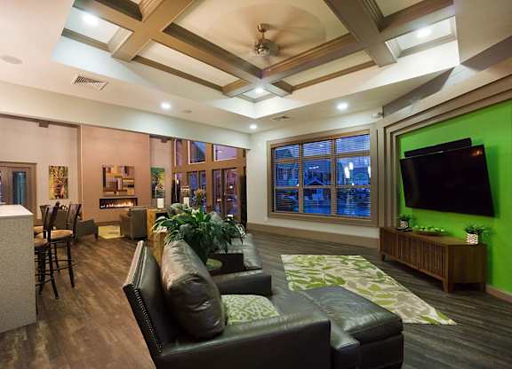 A living room with a black leather couch and a green screen on the wall.