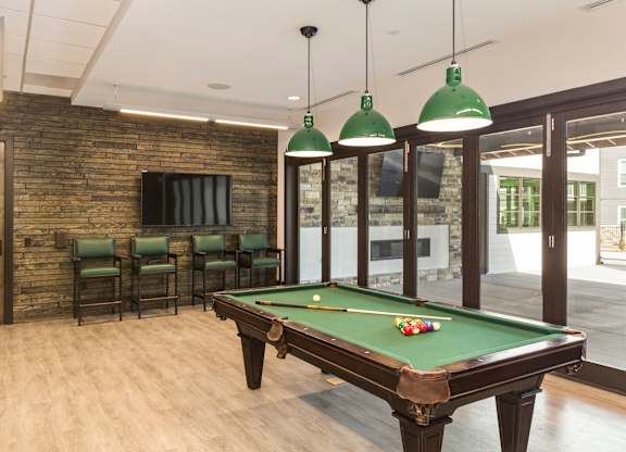 A pool table with green lampshades hanging from the ceiling.