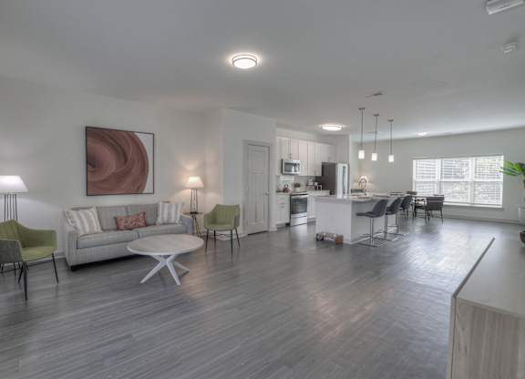 Three-Bedroom Luxury Apartments in East Nashville, TN - Flats at Laurel and Pine - Open Layout Living Room with Vinyl Plank Flooring, Couch, Armchairs, Round Coffee Table, Floor Lamp, Side Table with Lamp, and View of Kitchen.