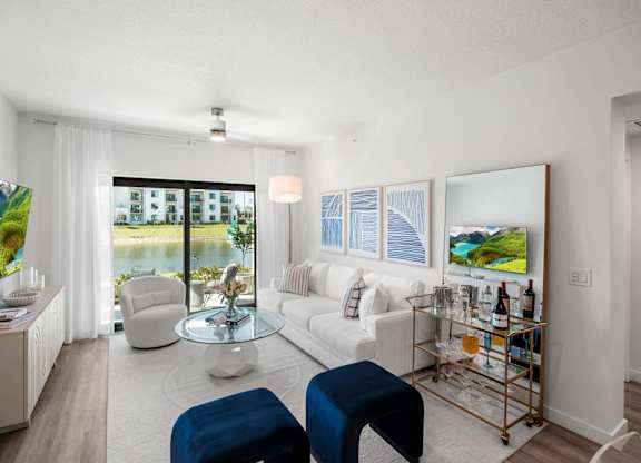 A living room with a white couch, a blue ottoman, and a glass coffee table.
