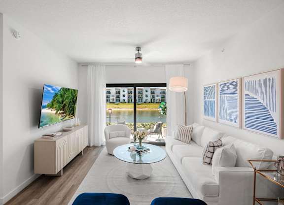 A living room with a television, a sofa, a coffee table, and a window overlooking a body of water.