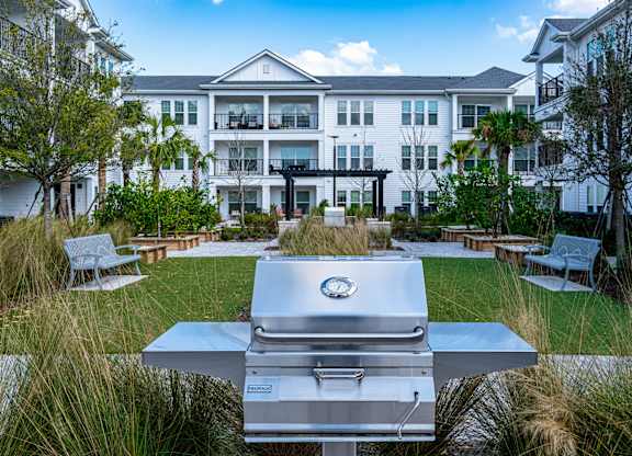 A silver grill is in the foreground of a grassy area in front of a white building.