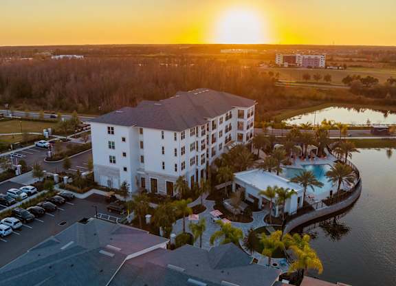 A large white hotel with a pool and a sunset in the background.