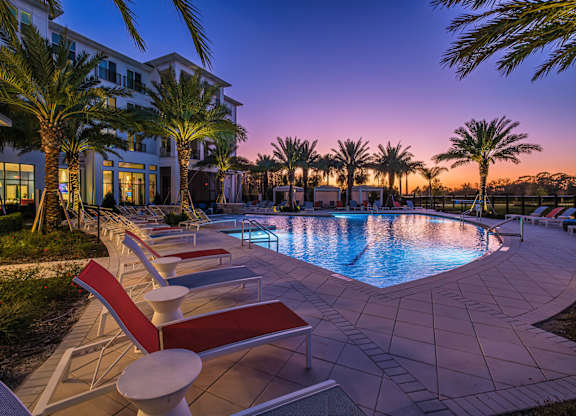 A pool surrounded by palm trees and lounge chairs.