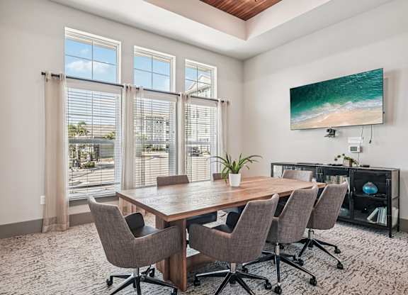 A conference room with a large table and chairs, a television, and a view of the outside through the windows.
