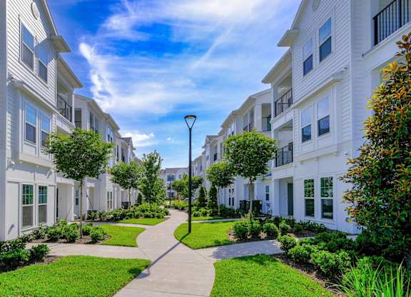 a walkway between two apartment buildings with green grass and trees at Altis Grand Lake Willis, Orlando Florida