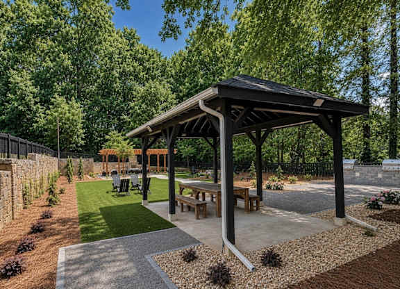A wooden pavilion is surrounded by a gravel and grass area.