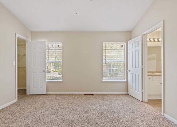 A room with a carpeted floor and two windows.