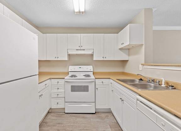 A white kitchen with a refrigerator, oven, and sink.