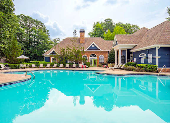 A large swimming pool in front of a house with a blue roof.