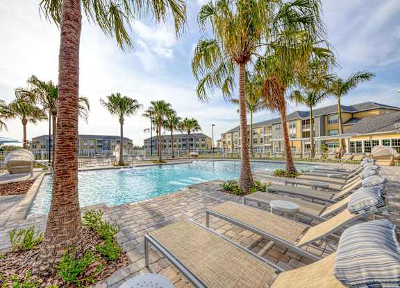 A pool surrounded by palm trees and lounge chairs.