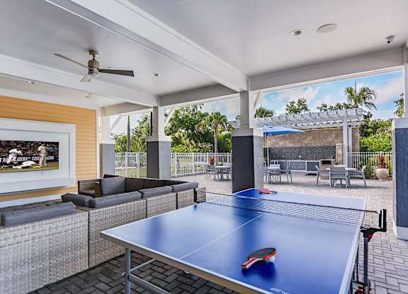 A ping pong table is in the middle of a room with a ceiling fan and a painting on the wall.