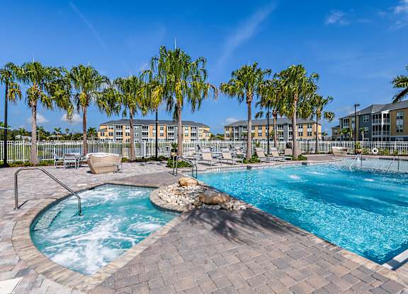A large outdoor swimming pool surrounded by palm trees and a hot tub.