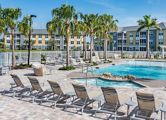 A pool surrounded by lounge chairs and palm trees.