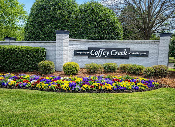 A sign that says Coffey Creek in front of a flower bed.