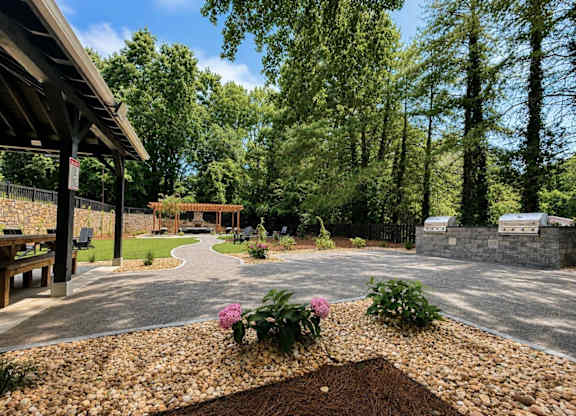 A garden with a gravel path and a bench under a wooden structure.