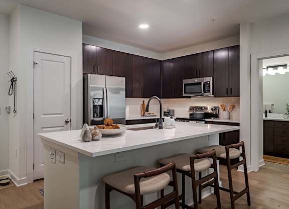 A kitchen with a white counter top and brown chairs.