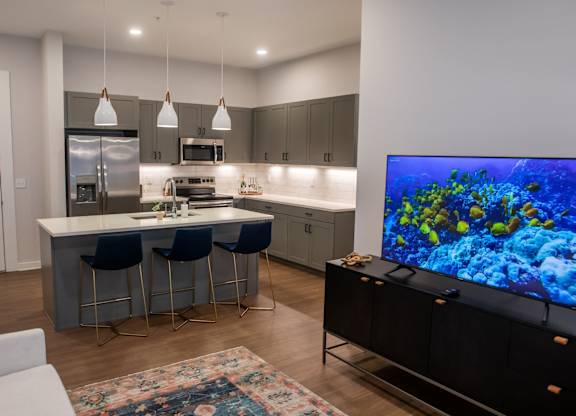 A modern kitchen with a bar area and a television displaying an underwater scene.
