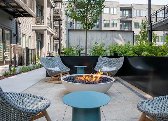 A fire pit sits in the middle of a patio surrounded by chairs.