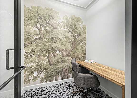 A room with a tree mural on the wall and a black chair in front of it.