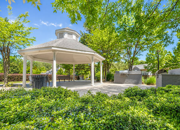 A gazebo is surrounded by green bushes.