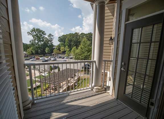 A balcony with a view of a parking lot and trees.