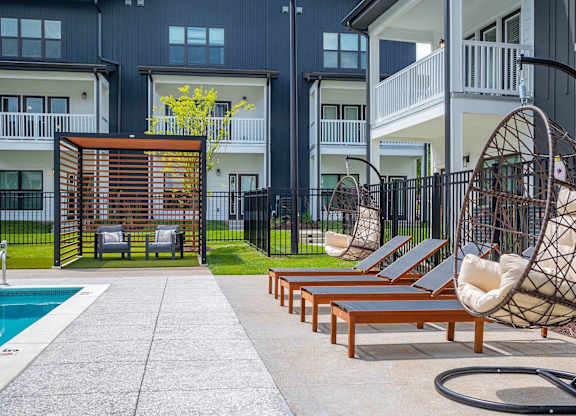 a patio with lounge chairs and a swing in front of an apartment building