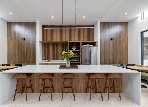 A modern kitchen with a long white island and wooden stools.