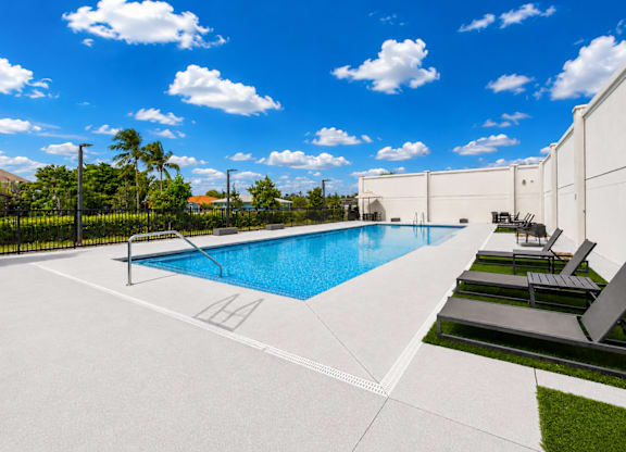 A swimming pool with lounge chairs and a white fence.