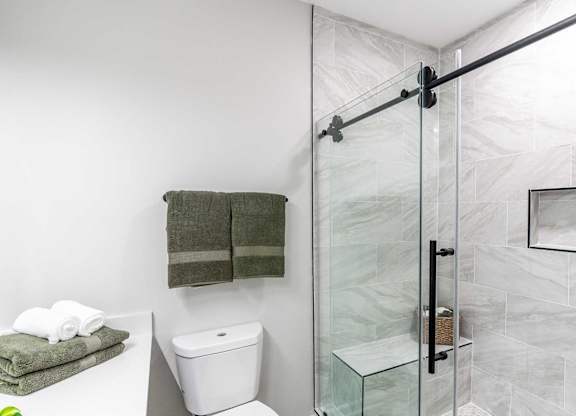 A bathroom with a toilet, a towel, and a glass shower door.
